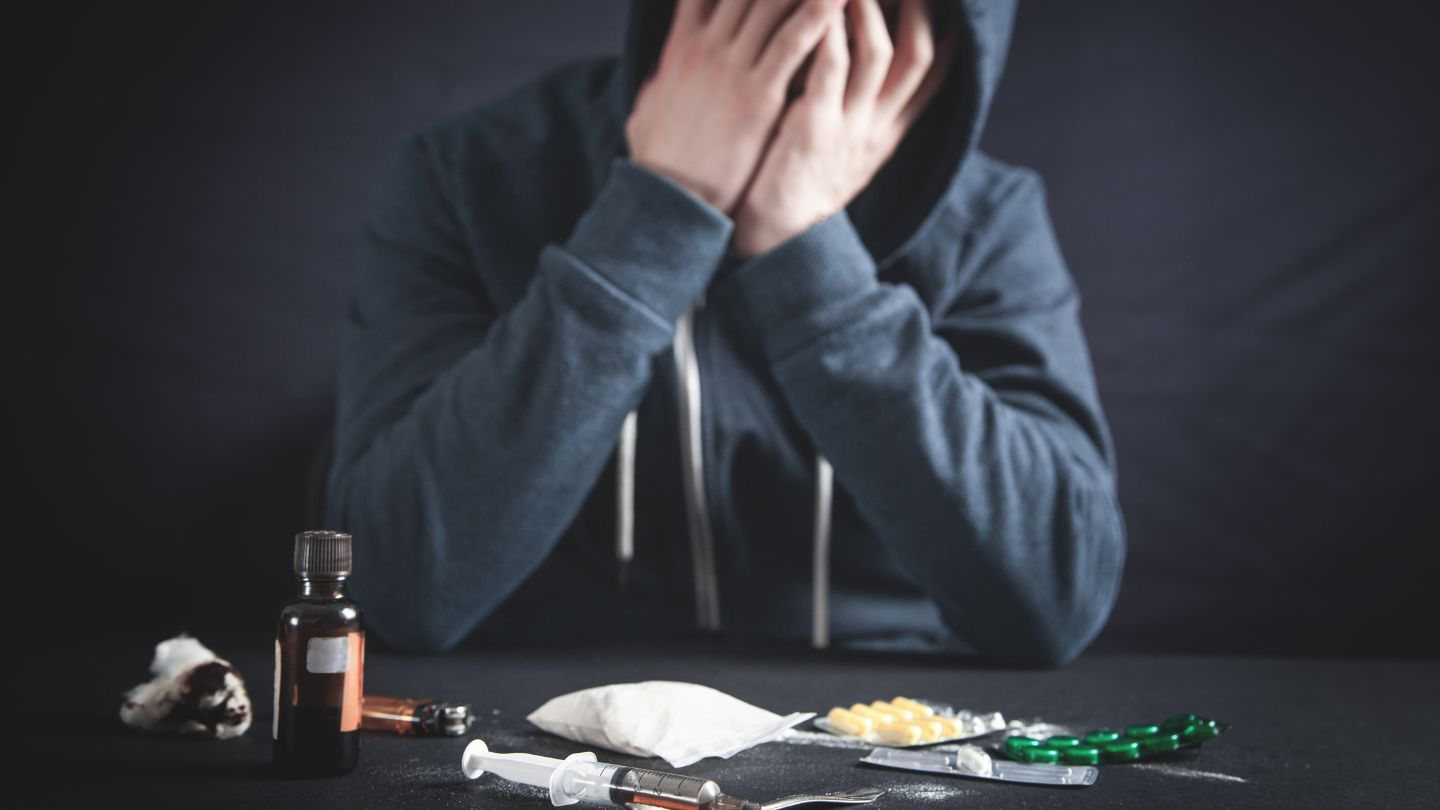 Person with Head in Hands Surrounded by Drugs on Table